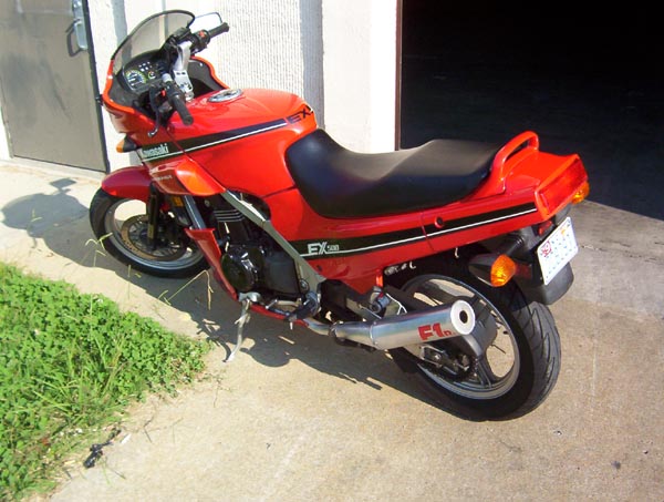 Red Kawasaki EX motorcycle with black seat and silver exhaust pipe, parked on concrete