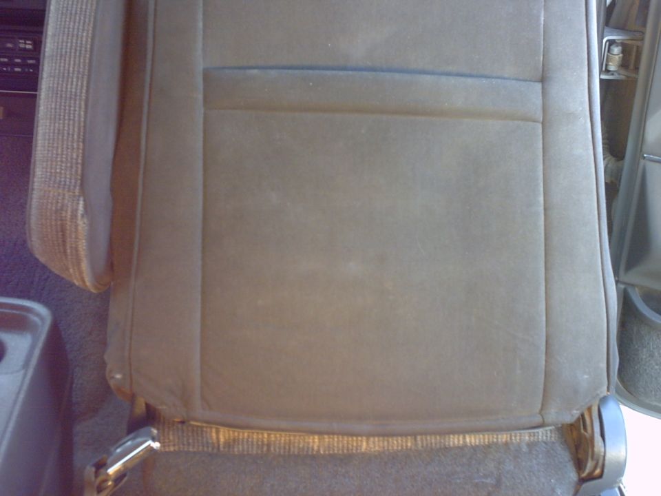 Car seat with worn fabric and visible stitching. A portion of the dashboard is visible on the left