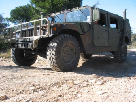 1996 Ford Bronco - Olive drab Humvee parked on a dirt road with trees in the background.
