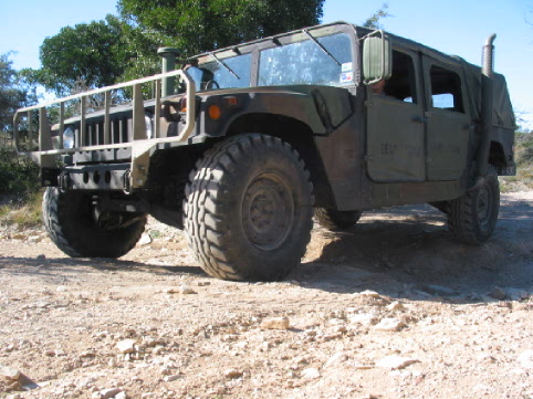 Olive drab Humvee with brush guard and large tires parked on a dirt road