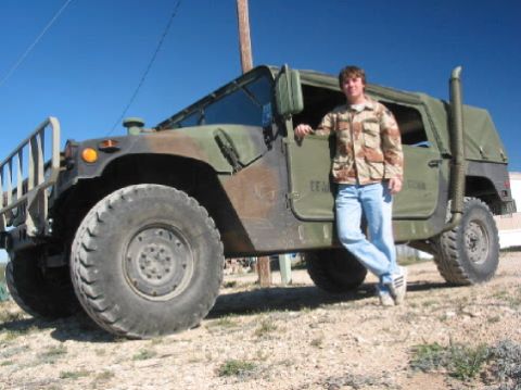 1996 Ford Bronco - A man poses next to a military-style Humvee under a clear blue sky.