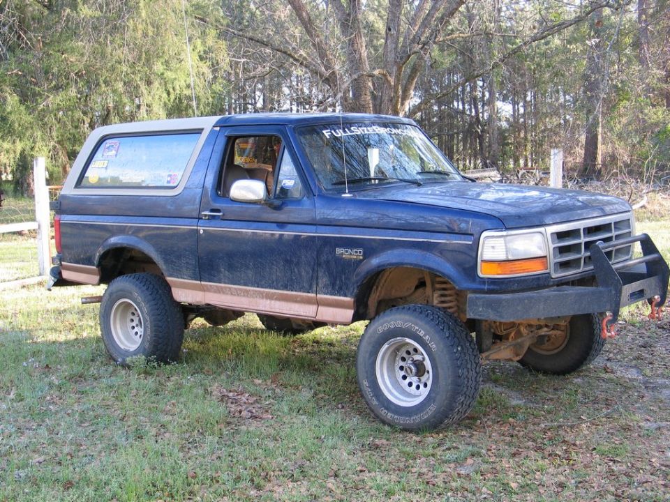 Blue Ford Bronco with aftermarket bumper and lifted suspension parked on grass