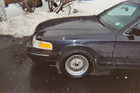 2000 Ford Crown Victoria - A dark blue 2000 Ford Crown Victoria is viewed from the front quarter angle on a wet day with snow visible.