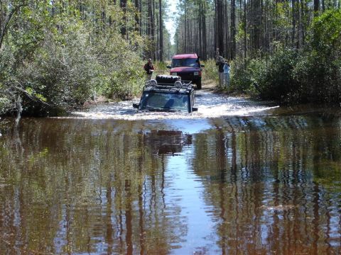 1992 Ford Bronco - Two SUVs navigate a water crossing in a wooded area.