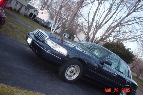 2000 Ford Crown Victoria - A dark sedan is parked on a driveway in front of a residential house. The photo has a date stamp.