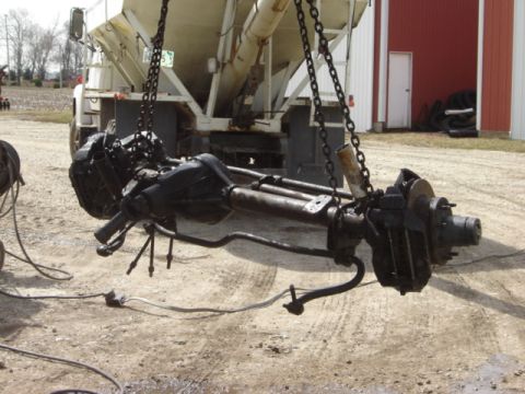 1992 Ford Bronco - A disassembled front axle assembly is suspended by chains, showing its mechanical components.