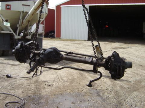 1992 Ford Bronco - Front and rear axles are suspended by chains, with a large truck and a red barn visible in the background.