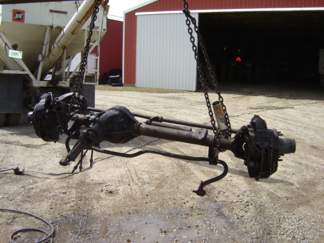 Front and rear axles lifted by chains, with a truck and barn in the background