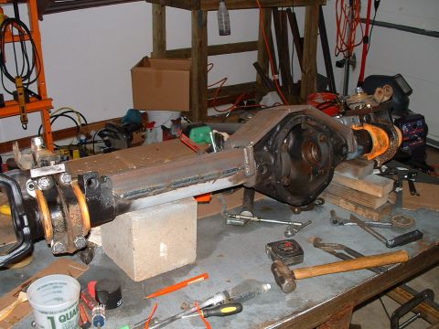 1995 Ford Bronco - A vehicle's axle assembly is shown in a garage setting with various tools and equipment nearby.