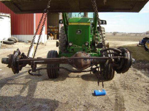 1992 Ford Bronco - Front axle assembly of a tractor is being lifted by a loader in front of a red barn.