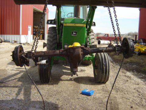 1992 Ford Bronco - A rear axle assembly is suspended by chains, with a tractor and a red pickup truck in the background.