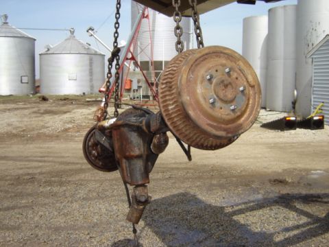 1992 Ford Bronco - A rusty rear axle assembly with a brake drum is suspended by chains in front of farm silos.