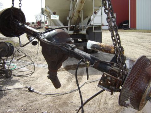 1992 Ford Bronco - A rusty rear axle assembly is suspended by chains, with a truck visible behind it.