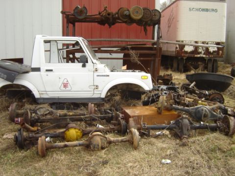 1992 Ford Bronco - Suzuki Samurai body sits amidst a collection of various axles and vehicle parts.