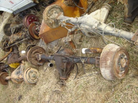 1992 Ford Bronco - Multiple vehicle axles are scattered on the ground, some with brake drums attached.