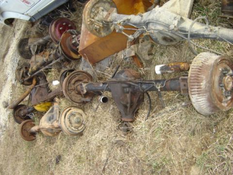 1992 Ford Bronco - A collection of assorted vehicle axles and brake drums are piled on the ground, appearing to be scrap parts.