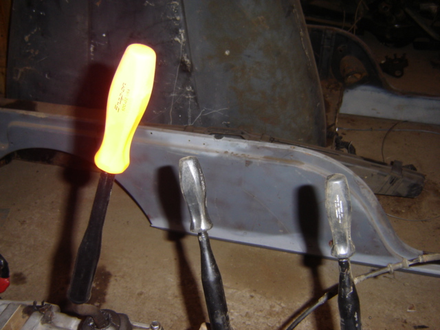 Yellow handled screwdriver and two other screwdrivers resting on a vehicle frame