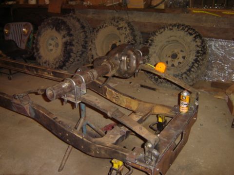1992 Ford Bronco - A vehicle frame is on jack stands with large tires and a Jeep grille visible in the background.