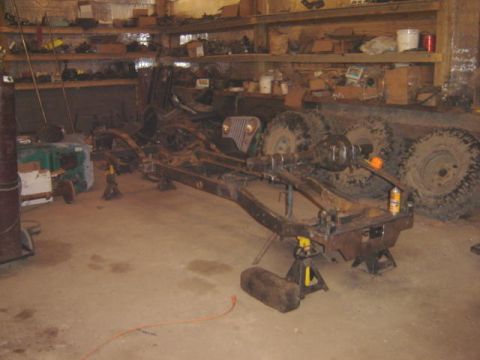 1992 Ford Bronco - A vehicle frame is supported by jack stands in a cluttered workshop environment.