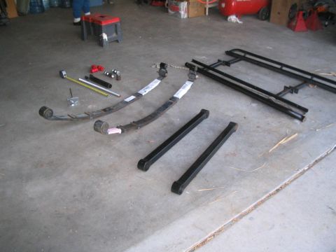 1991 Ford Bronco - Various automotive parts laid out on a concrete surface, including leaf springs and metal bars.