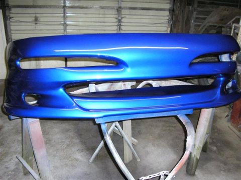 1994 Ford Probe - A freshly painted blue bumper is displayed on sawhorses in a garage.