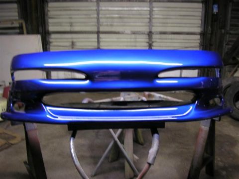 1994 Ford Probe - A freshly painted blue bumper is displayed on a stand in a workshop.