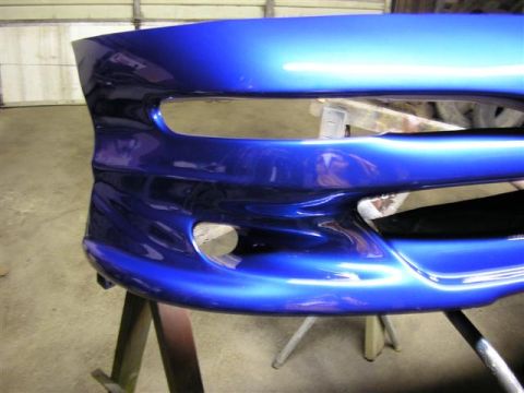 1994 Ford Probe - A freshly painted blue car bumper is mounted on sawhorses in a garage.