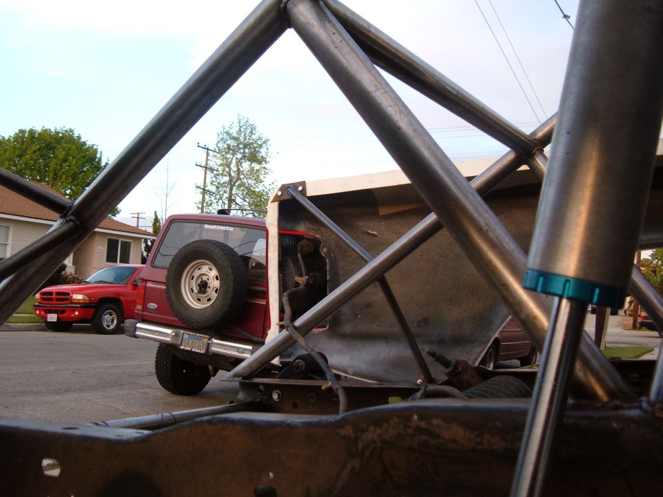 Red pickup truck's rear with spare tire, seen from behind a roll cage