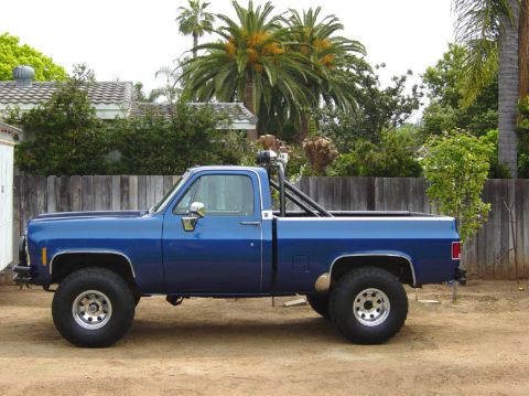 1979 Chevrolet C/K Pickup - Side view of a blue pickup truck with a roll bar and lifted suspension, parked outdoors.