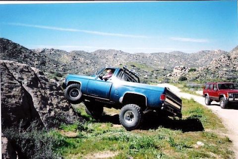 1979 Chevrolet C/K Pickup - A blue 1979 Chevrolet C/K Pickup navigates a rocky trail, with a red SUV visible in the background.