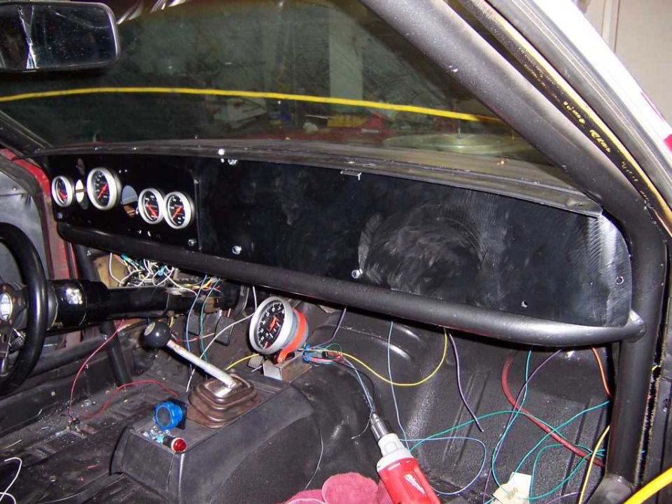 Custom flat black dash with white-face gauges and a shift-light tach in a stripped race-car interior