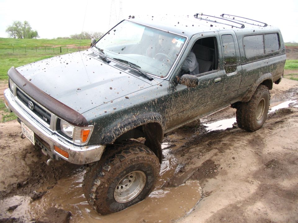 Mud-splattered green Toyota pickup with shell flexing in a deep muddy rut