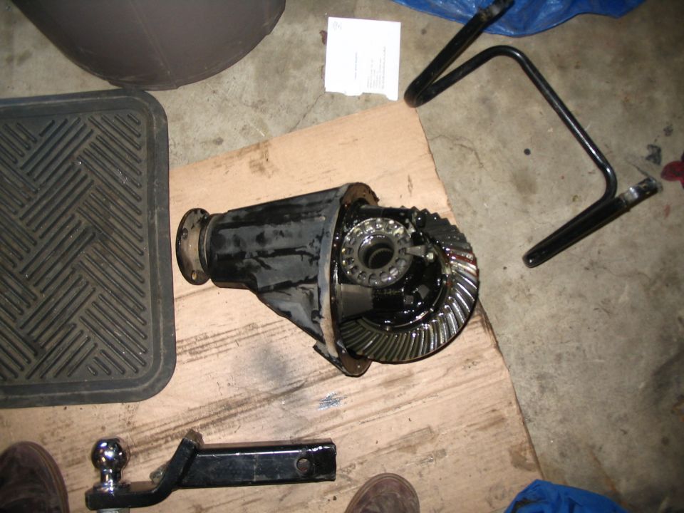 Vehicle differential third member with ring gear on plywood in garage, tools nearby