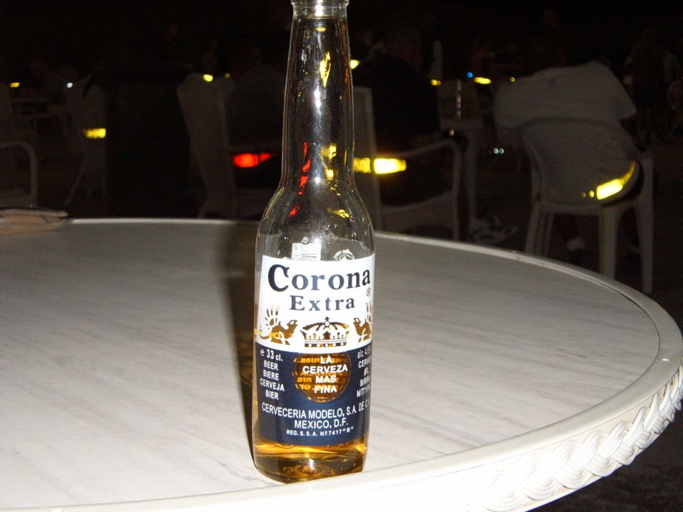 Corona Extra bottle on a white table, with blurred background lights and people