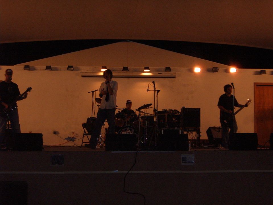 Band performing on stage with guitars and drums, dimly lit