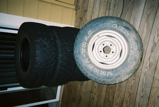 Stack of four tires, one with a white rim and General Grabber AT2 tires