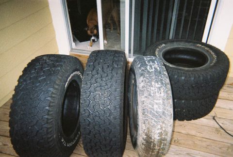 1988 Ford Bronco - Four unmounted BFGoodrich All-Terrain T/A tires with raised white lettering stood on edge on a wood deck, showing chunky all-terrain tread…