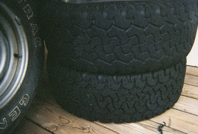 Two tires stacked on top of each other, with a third tire visible on the left. Some text is visible on the left tire