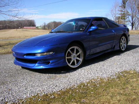 1994 Ford Probe - A blue 1994 Ford Probe is parked on a gravel driveway under a clear blue sky.