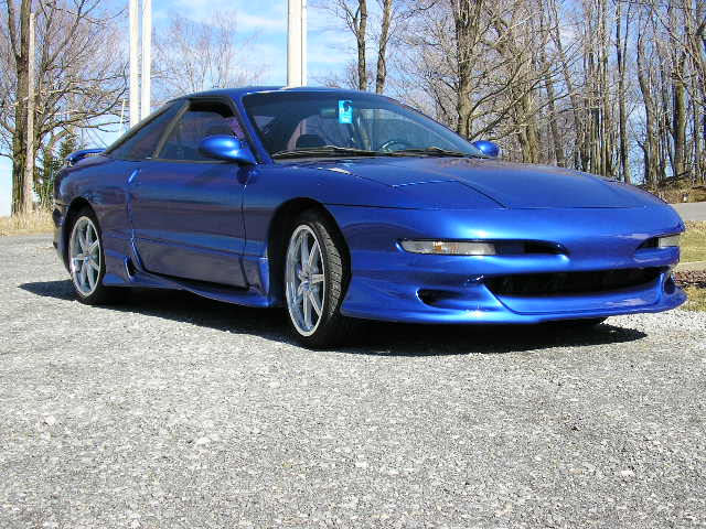 Blue 1994 Ford Probe GT coupe, front 3/4 view, custom body kit, aftermarket wheels, parked on gravel