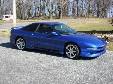 1994 Ford Probe - This blue 1994 Ford Probe is captured in a 3q front view, parked on a gravel surface with trees in the background.