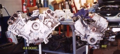 1996 Ford Bronco - Two V8 engines, one labeled 4.6 DOHC and the other 302, are displayed in a workshop setting.