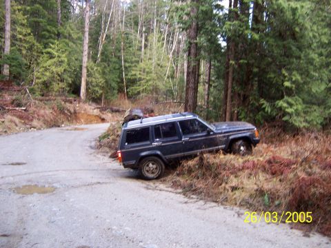 1987 Jeep Cherokee - Jeep Cherokee parked on a dirt road, partially off-road in brush.