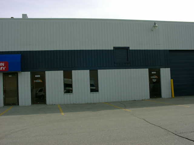 Building with blue and white siding, dark blue stripe, and multiple doors and windows. A yellow pole is visible near a large dark garage door