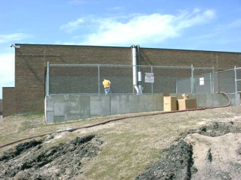 1999 Jeep Grand Cherokee - Industrial scene with large blower pipes and a worker in a yellow shirt standing behind a fence.