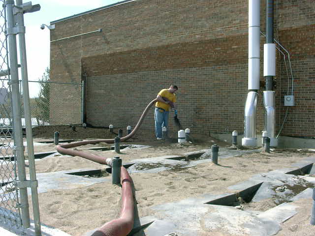 worker using a hose on a construction site with pipes and sand