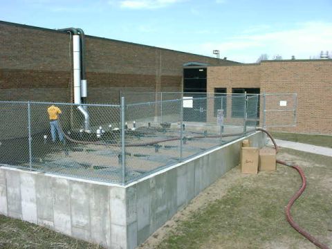 1999 Jeep Grand Cherokee - An industrial scene shows a person working near pipes behind a fence, with two boxes on the lawn.