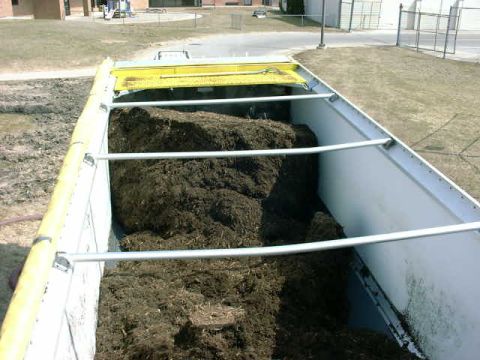 1999 Jeep Grand Cherokee - The interior of a dump truck bed loaded with a large pile of dark mulch, with a yellow tarp covering part of the load.