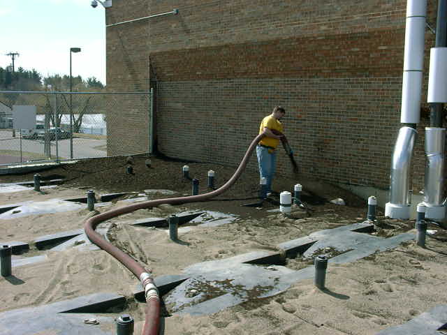 Worker using a hose on a construction site with a brick building and pipes
