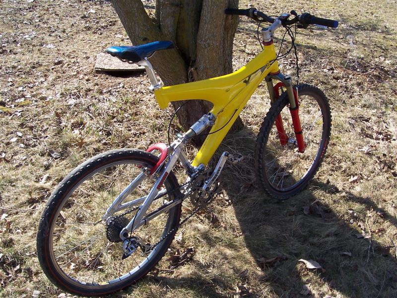 Yellow full-suspension mountain bike leaning against a tree on a lawn.